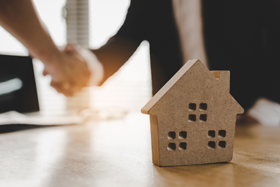 two people shaking hands with a model of a home in front of them